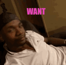 a man in a white shirt is laying on a couch with the word want behind him