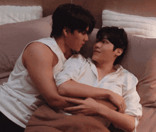 two men are hugging each other on a bed with pink pillows