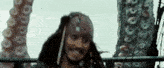 jack sparrow from pirates of the caribbean is smiling while standing next to a large octopus .