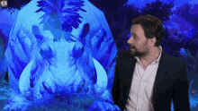 a man in a suit and white shirt stands in front of a large blue monster