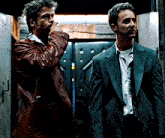 a man in a suit smoking a cigarette next to another man