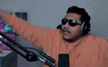 a man wearing sunglasses and headphones is standing in front of a microphone and pointing .