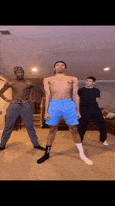 a shirtless man in blue shorts is standing in front of two other men