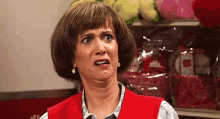 a woman in a red vest is making a funny face in front of a shelf of stuffed animals .
