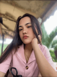 a young woman in a pink shirt is sitting at a table with her hand on her chin