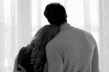 a man and a woman hugging each other in front of a window