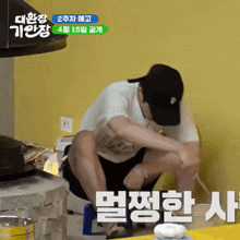 a man squatting down in front of a yellow wall with korean writing on the bottom