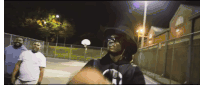 a man wearing a hat and sunglasses stands in front of a basketball hoop