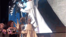 a woman in a white dress is standing on a stage holding a trophy .