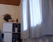 a room with white curtains and a shelf with a statue on top