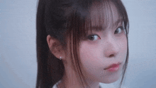 a close up of a young girl 's face with a ponytail and bangs looking at the camera .
