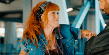 a woman with red hair wearing a bandana and a denim jacket holds a man 's hand
