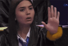 a woman in a graduation gown holds her hand up in front of her face