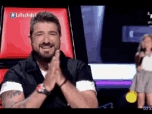 a man with a beard is smiling in front of a red chair that says lavozkids1