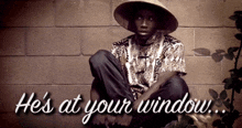 a man in a hat sits in front of a brick wall with the words he 's at your window above him