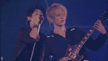 two men singing in front of a blue background with the letter d in the corner