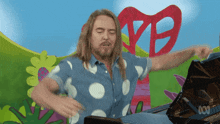 a man in a polka dot shirt is playing a piano in front of a sign that says vb