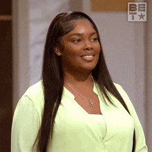a woman in a green shirt stands in front of a sign that says be on it