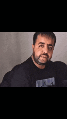 a man with a beard is wearing a black shirt with a blue graphic on it