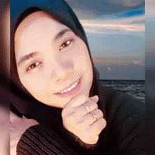 a woman wearing a black sweater and a hijab is smiling