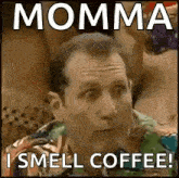 a man is sitting in front of a group of women and making a funny face while smelling coffee .