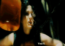 a woman in a black tank top is talking to someone in a dark room while holding a jar of liquid .