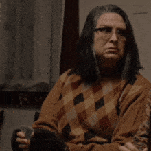 a woman wearing glasses and a plaid sweater holds a card in her hand