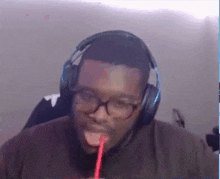a man wearing headphones and glasses is drinking from a straw .