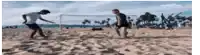 two men are playing soccer on a sandy beach with a blurred background