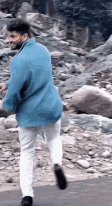a man wearing a blue jacket and white pants is walking on a rocky road .