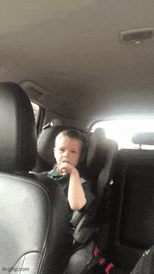 a young boy is sitting in a car seat looking at the camera .