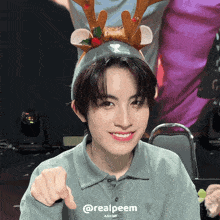 a young man wearing a reindeer headband points at the camera with the hashtag @realpeem