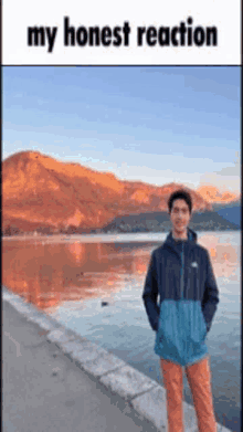 a man is standing next to a lake with mountains in the background .