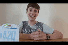 a young boy sitting at a table with a sign that says 8:20 on it