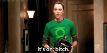 a man wearing a green lantern shirt is holding a black object and saying `` it 's on , bitch . ''
