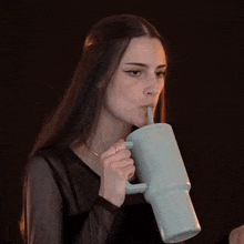 a woman with long hair is drinking from a mug with a straw .