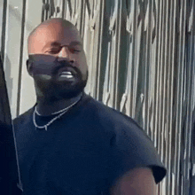 kanye west is wearing a black shirt and a necklace while standing in front of a fence .