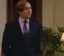 a man in a suit and tie is standing in front of a plant