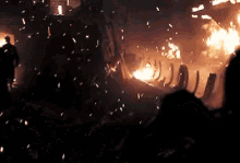 a group of people are standing in front of a burning building at night .