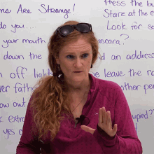 a woman wearing sunglasses stands in front of a white board that says strange