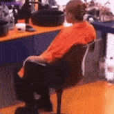 a man in an orange shirt sits in a chair