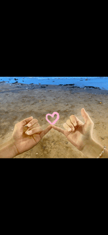 a couple making a pink heart with their fingers on a beach