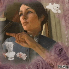 a woman is pointing at a statue of a woman in a painting surrounded by roses and a cat .