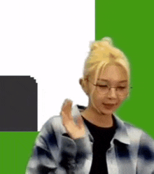 a woman wearing glasses and a plaid shirt is waving her hand in front of a green background .
