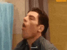 a man is yawning in front of a shower curtain while looking at himself in the mirror .