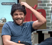 a man is sitting on a couch and scratching his head while smiling .