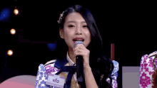 a woman is holding a microphone in front of a white sign that says ' a ' on it