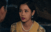 a woman wearing a pearl necklace and earrings looks to the side