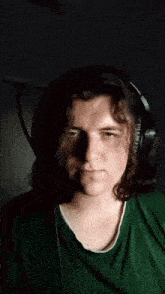 a young man wearing headphones and a green shirt looks at the camera