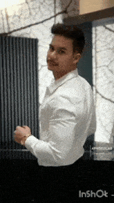 a man wearing a white shirt and black pants is standing in front of a window